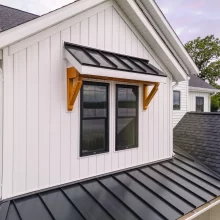 Close-up of window with black metal awning and wood bracket accents, standing-seam metal roof detail