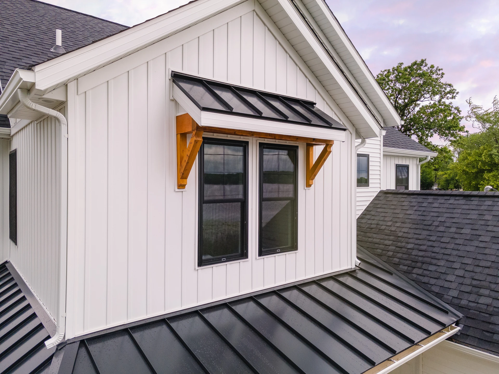Close-up of window with black metal awning and wood bracket accents, standing-seam metal roof detail