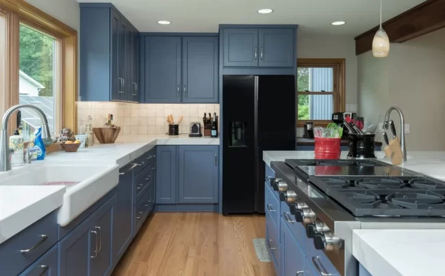Cooper Township Blue Kitchen Remodel | Pennings & Sons Remodeled kitchen with blue cabinets, farmhouse sink, black refrigerator, island cooktop, white countertops, and wood flooring