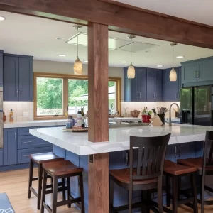 Custom kitchen with blue cabinetry, large white island, wood support posts, pendant lighting, bar seating, and stainless steel appliances