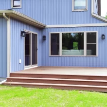 Backyard maintenance-free deck with wide steps, blue house siding, sliding glass door, exterior lighting, and grassy yard