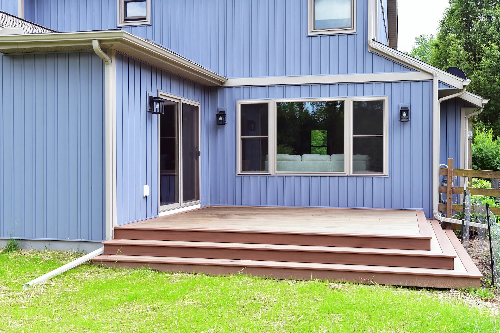 Backyard maintenance-free deck with wide steps, blue house siding, sliding glass door, exterior lighting, and grassy yard