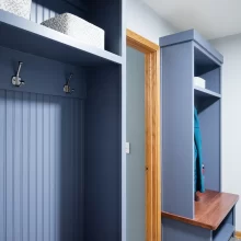 Custom blue mudroom lockers with wood bench seats, beadboard backing, coat hooks, upper storage shelves, and gray tile flooring