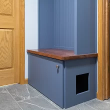 Custom blue mudroom bench with wood seat, cabinet storage, beadboard backing, gray tile floor, and built-in litter box opening