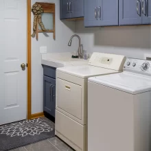 Mudroom laundry area with blue storage cabinets, utility sink, washer and dryer, gray tile floor, and wood door trim
