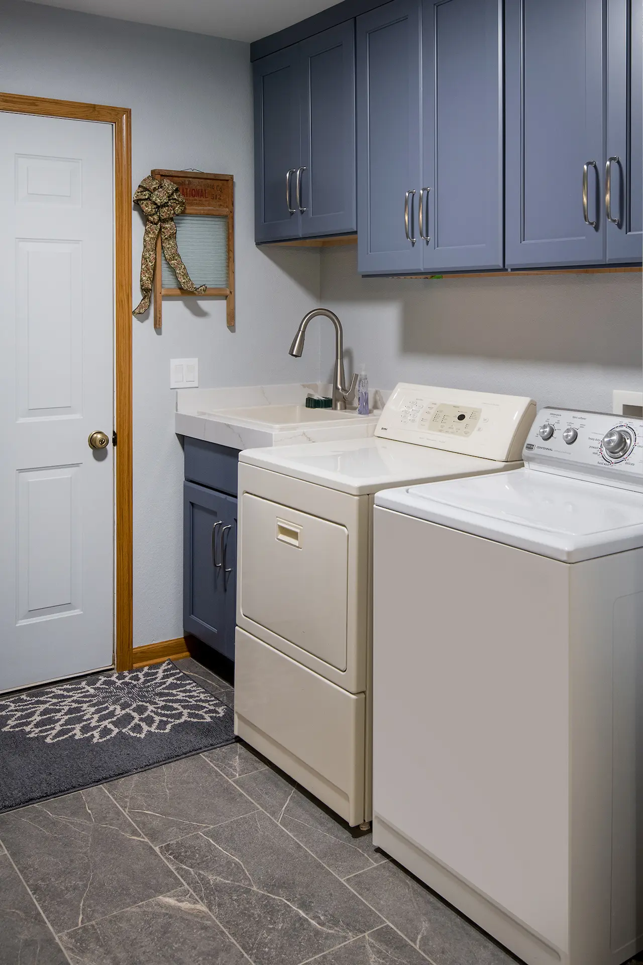 Mudroom laundry area with blue storage cabinets, utility sink, washer and dryer, gray tile floor, and wood door trim