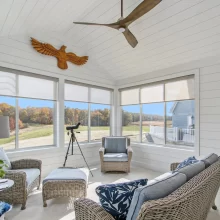 All-season sun room in a Galesburg custom home with vaulted shiplap ceiling, wicker seating, large windows and countryside views.