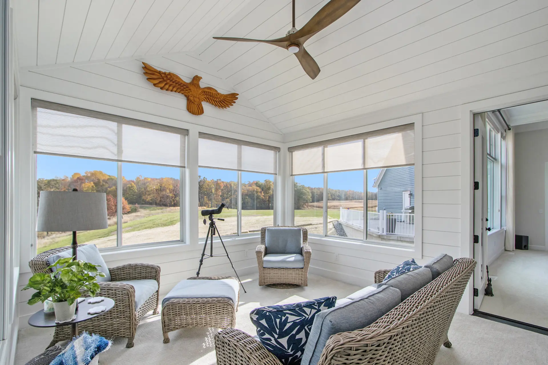 All-season sun room in a Galesburg custom home with vaulted shiplap ceiling, wicker seating, large windows and countryside views.
