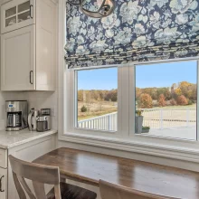 Coffee nook in a Galesburg custom home with built-in cabinetry, marble-style countertop, wood table, floral window shade and countryside view.