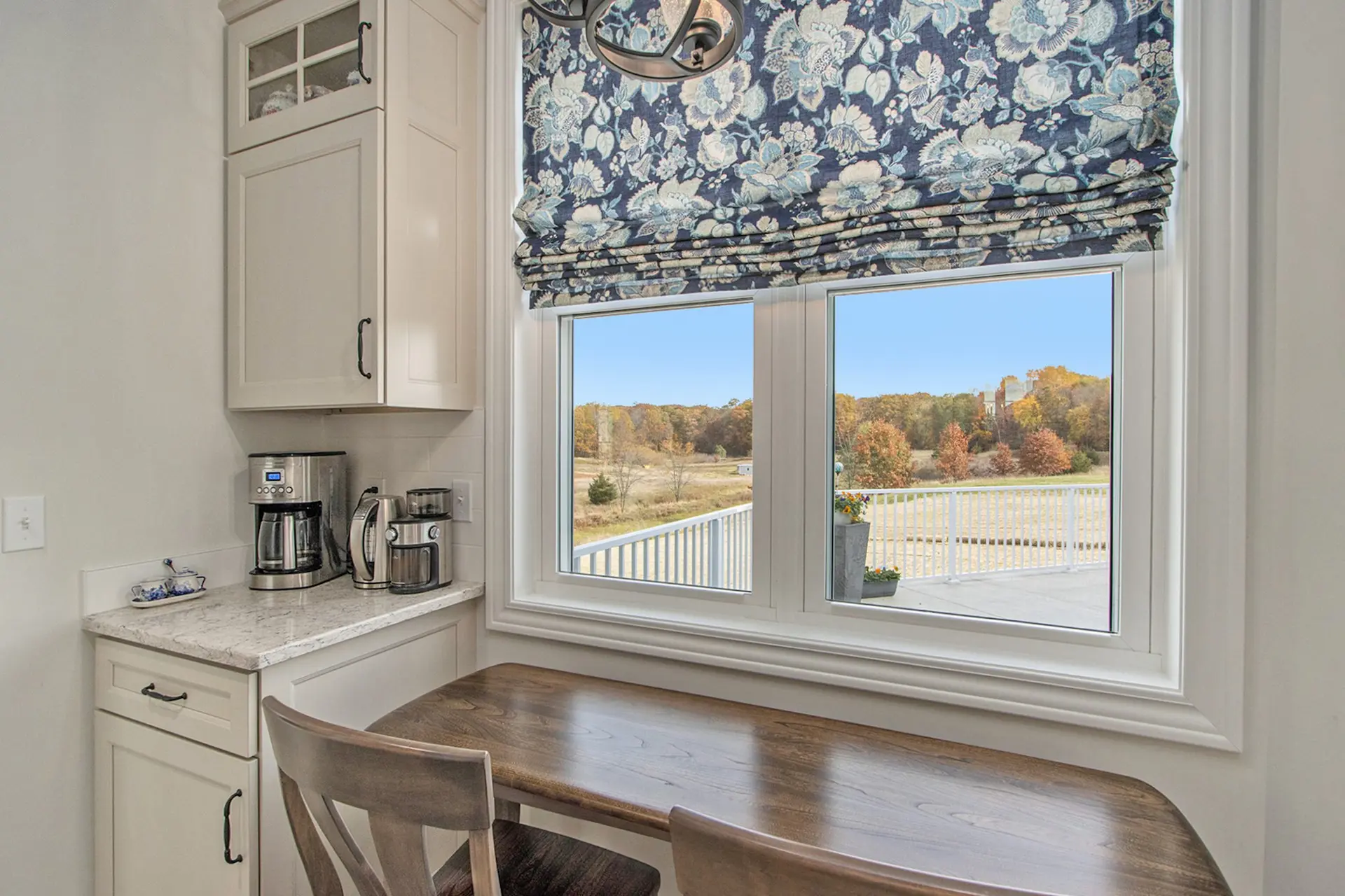 Coffee nook in a Galesburg custom home with built-in cabinetry, marble-style countertop, wood table, floral window shade and countryside view.