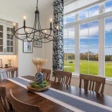 Dining room in a Galesburg custom home with wood table, chandelier, built-in cabinetry, large windows, floral curtains and countryside views.