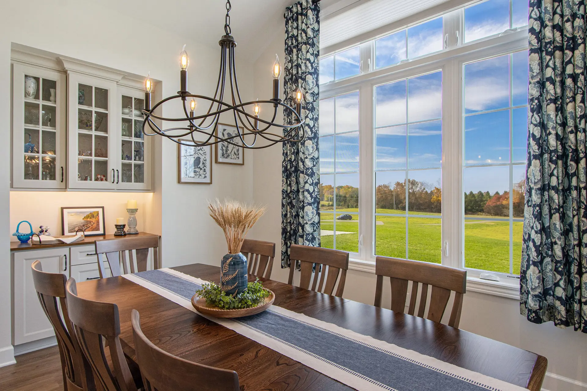 Dining room in a Galesburg custom home with wood table, chandelier, built-in cabinetry, large windows, floral curtains and countryside views.