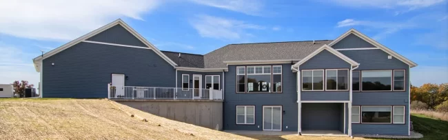 Rear Exterior of Galesburg Custom Home | Pennings & Sons Rear view of a blue Galesburg custom home with large windows, walkout lower level, raised deck and sloped backyard.