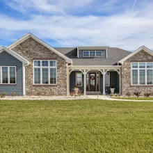 Front exterior of a Galesburg custom home with blue siding, stone accents, large windows and covered entry.