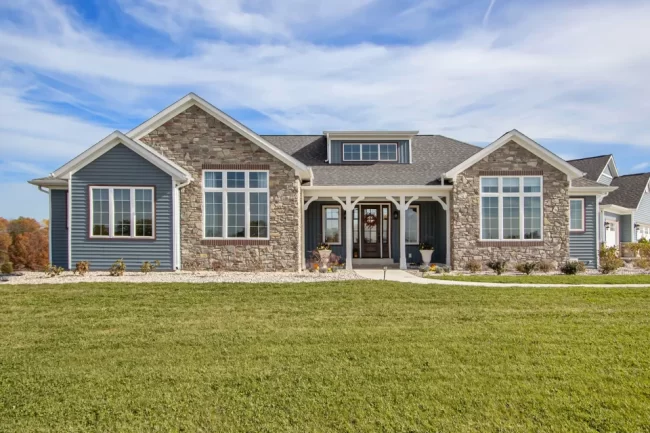 Front exterior of a Galesburg custom home with blue siding, stone accents, large windows and covered entry.