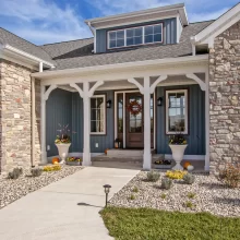 Covered front entry of a Galesburg custom home with stone columns, wood front door, white trim and landscaped walkway.