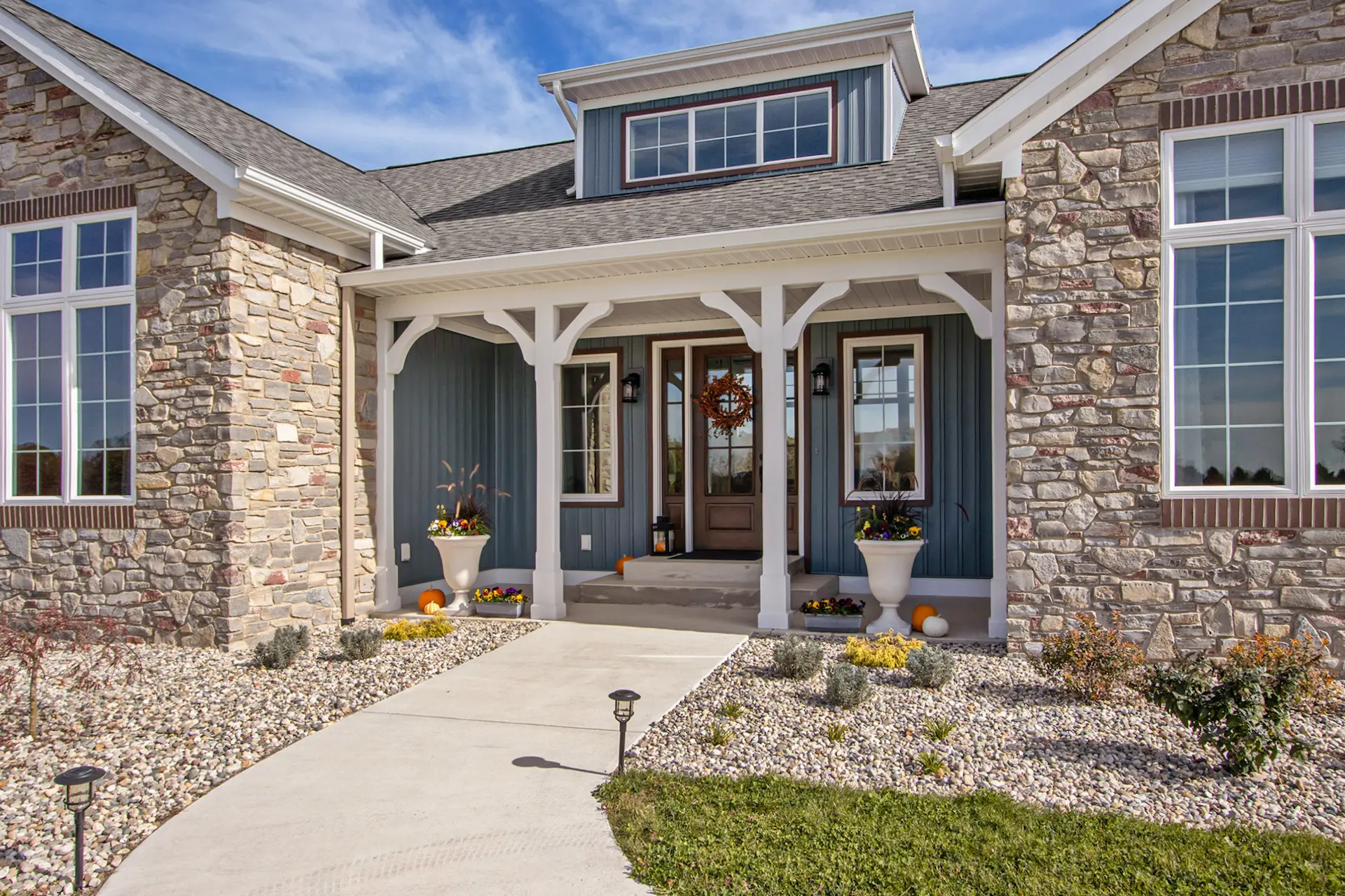 Covered front entry of a Galesburg custom home with stone columns, wood front door, white trim and landscaped walkway.