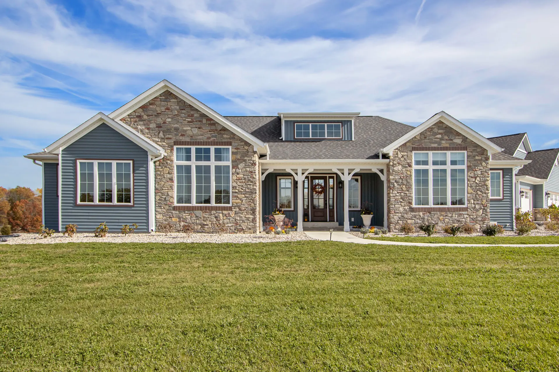 Front exterior of a Galesburg custom home with blue siding, stone accents, large windows and covered entry.