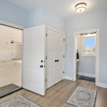 Garage entrance in a Galesburg custom home with blue walls, white trim, built-in storage, wood-look flooring and nearby bathroom.