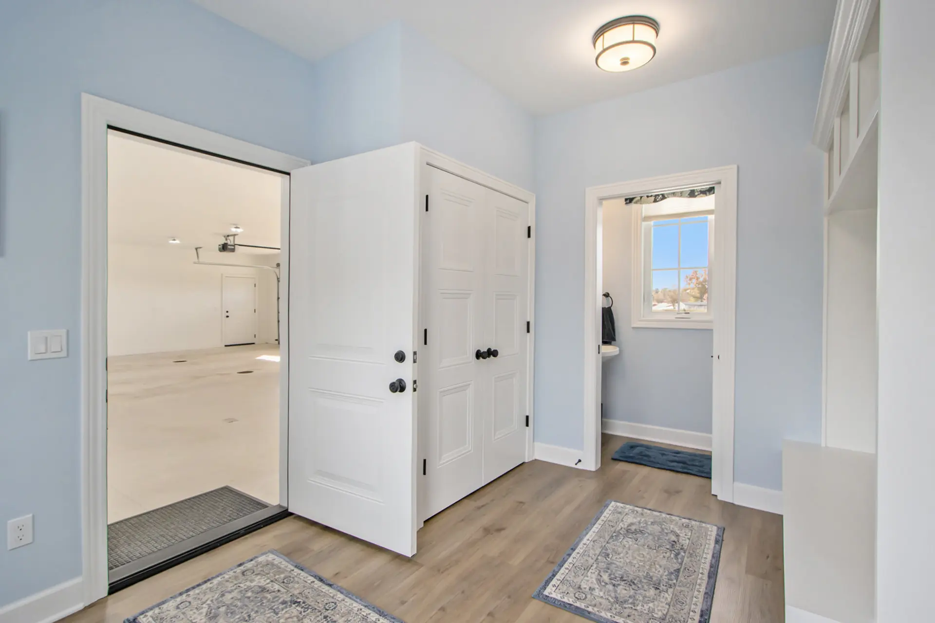 Garage entrance in a Galesburg custom home with blue walls, white trim, built-in storage, wood-look flooring and nearby bathroom.