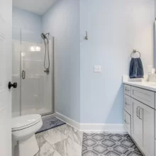 Guest bathroom in a Galesburg custom home with glass shower, light blue vanity, blue walls, marble-style floor tile and modern fixtures.
