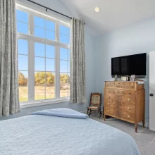 Guest bedroom in a Galesburg custom home with blue bedding, vaulted ceiling, large windows and countryside views.
