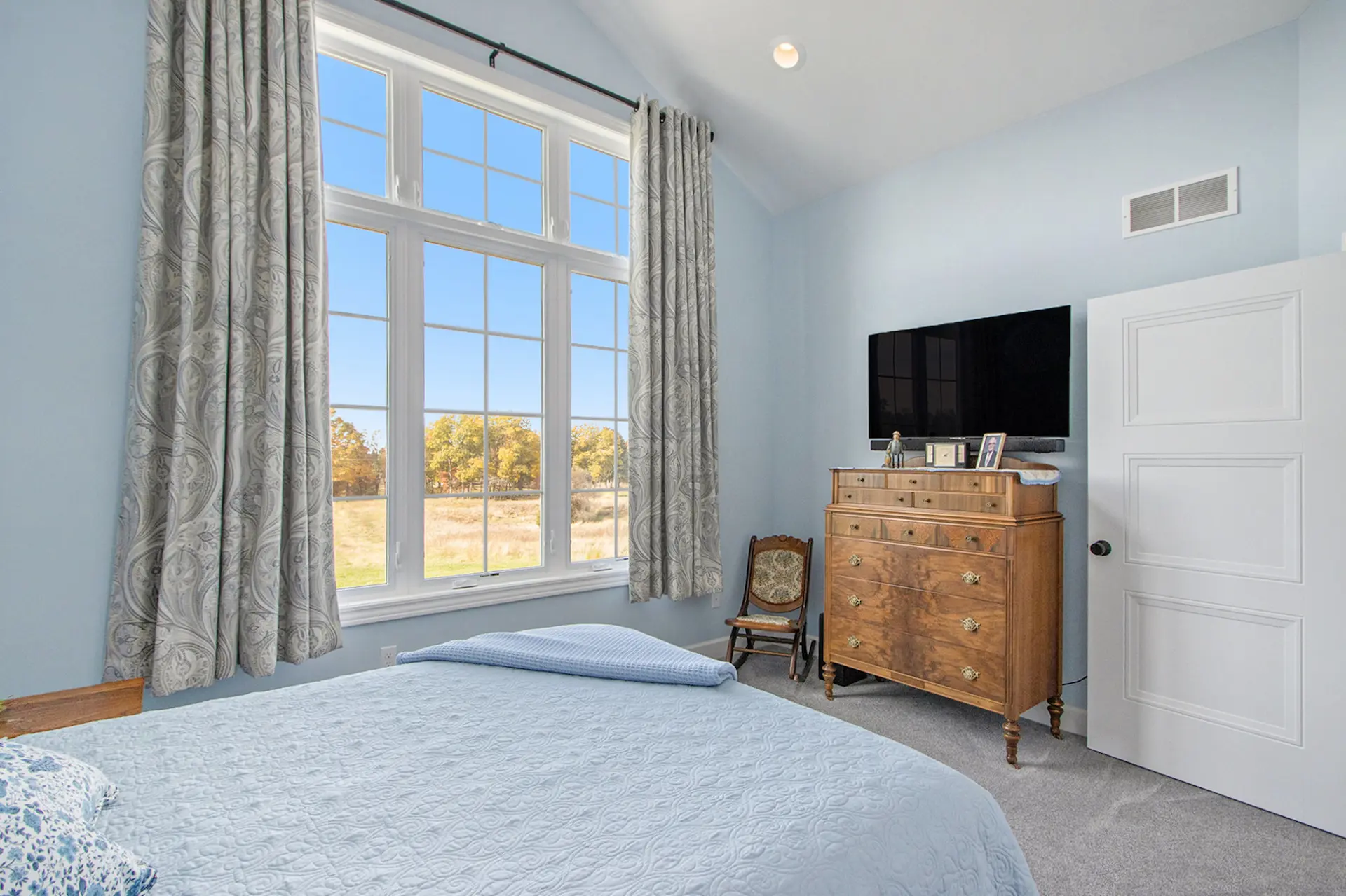 Guest bedroom in a Galesburg custom home with blue bedding, vaulted ceiling, large windows and countryside views.