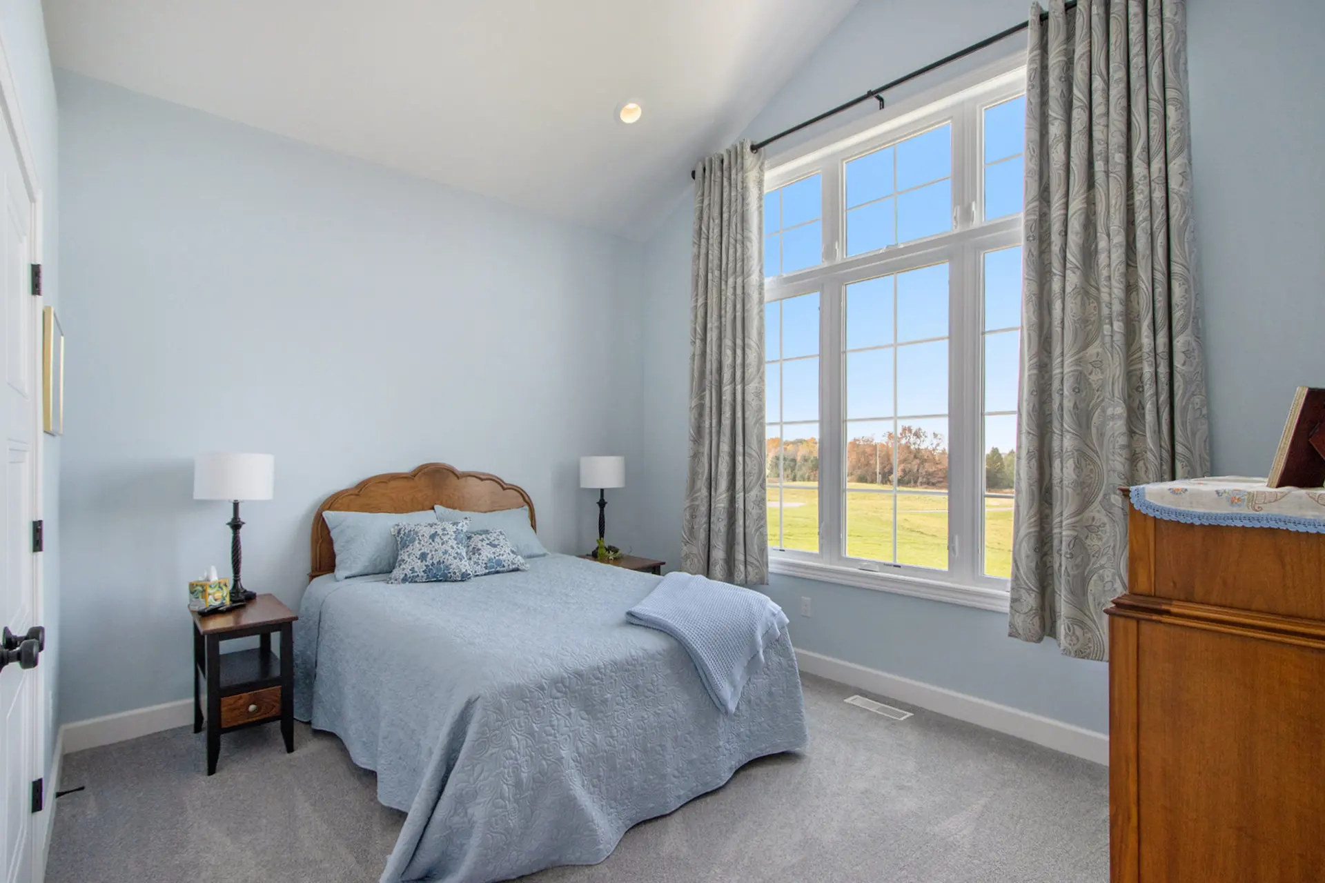 Guest bedroom in a Galesburg custom home with blue bedding, vaulted ceiling, large windows and countryside views.