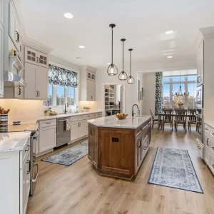 Bright custom kitchen with white cabinetry, wood island, pendant lights, marble-style counters and open dining area.
