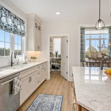 Custom kitchen in a Galesburg home with white cabinetry, marble-style island, walk-in pantry, pendant lights and view into the dining room.