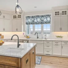 Bright custom kitchen with white cabinetry, wood island, pendant lights, marble-style counters and open dining area.