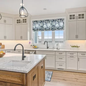 Bright custom kitchen with white cabinetry, wood island, pendant lights, marble-style counters and open dining area.