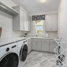 Laundry room in a Galesburg custom home with light blue cabinetry, washer and dryer, marble-style counters, sink and tile flooring.
