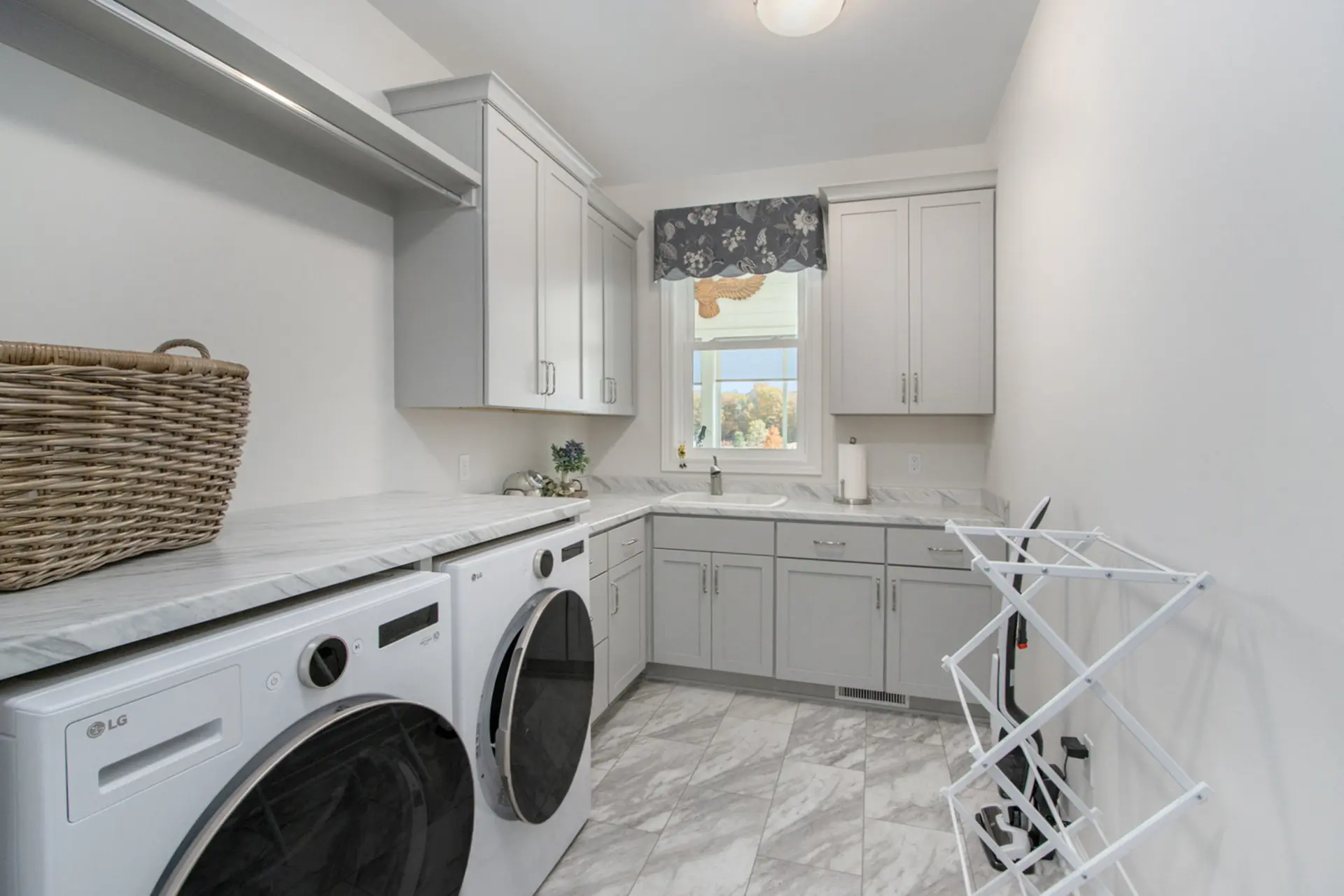 Laundry room in a Galesburg custom home with light blue cabinetry, washer and dryer, marble-style counters, sink and tile flooring.