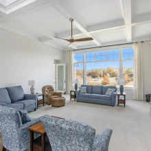Bright living room in a Galesburg custom home with coffered ceiling, large windows, blue seating, built-in media wall and countryside views.