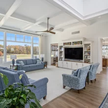 Open living room with coffered ceiling, built-in entertainment center, large windows and view into the custom kitchen.