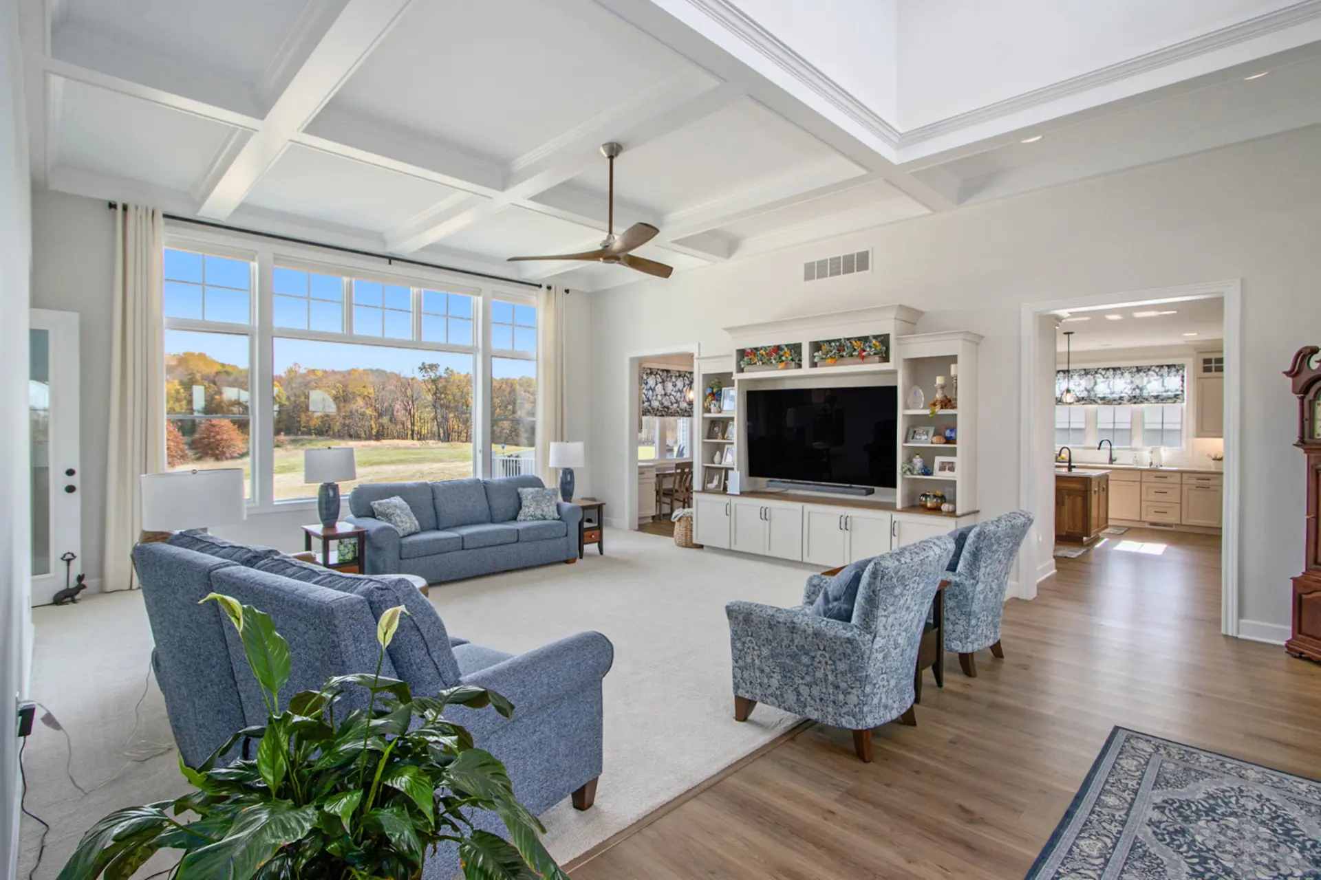 Open living room with coffered ceiling, built-in entertainment center, large windows and view into the custom kitchen.