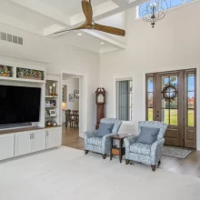 Living room with built-in media wall, blue accent chairs, vaulted ceiling, ceiling fan and front entry with wood doors.