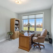 Home office with wood desk, built-in bookcase, soft green walls, large window and countryside view.