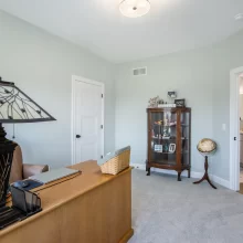 Home office angle showing wood desk, display cabinet, globe, soft green walls and doorway to a nearby bathroom.