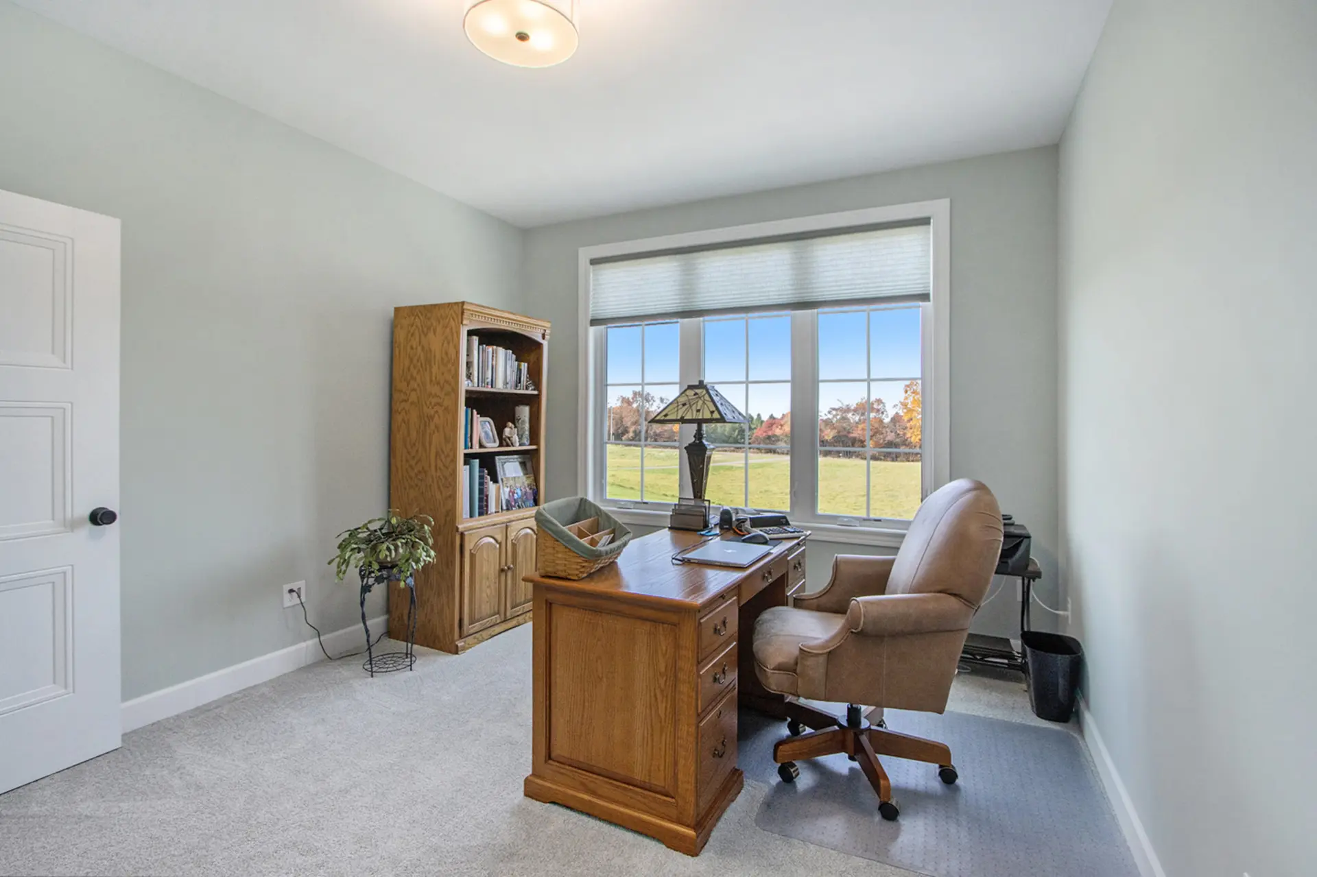 Home office with wood desk, built-in bookcase, soft green walls, large window and countryside view.
