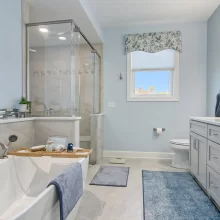 Primary bathroom with freestanding soaking tub, glass tile shower, gray vanity, blue accents and large window.