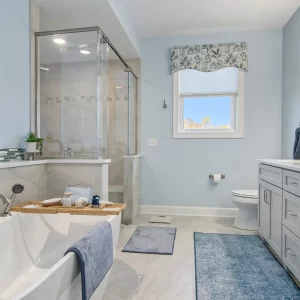 Primary bathroom with freestanding soaking tub, glass tile shower, gray vanity, blue accents and large window.