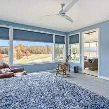 Primary bedroom with blue walls, large windows, countryside views, ceiling fan, sitting area and access to a screened porch.