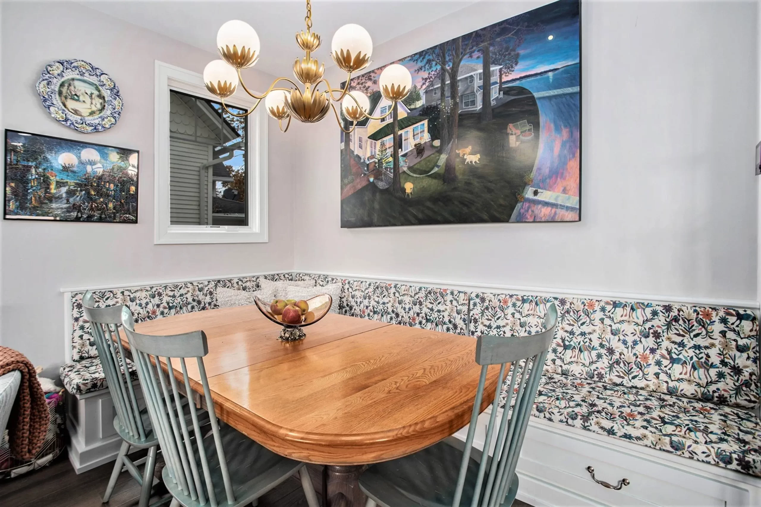 Breakfast nook with built-in floral banquette, wood dining table, statement chandelier, artwork, and lake-inspired décor