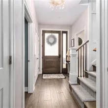 Bright foyer with wood-look flooring, paneled doors, staircase, carpet runner, and glass front entry door
