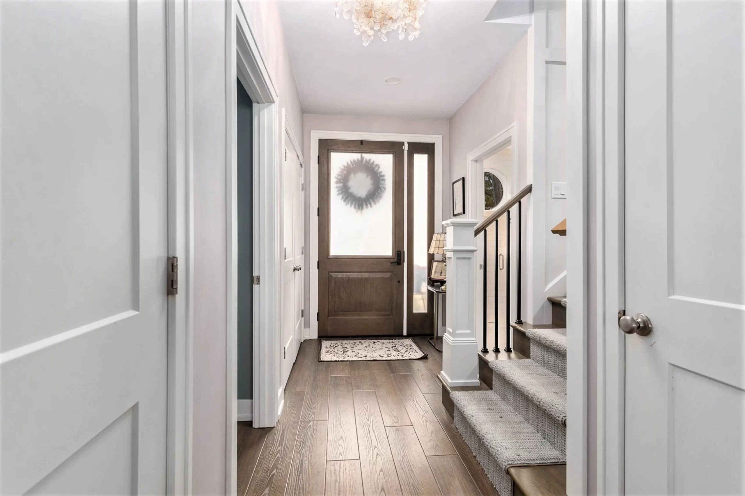 Bright foyer with wood-look flooring, paneled doors, staircase, carpet runner, and glass front entry door