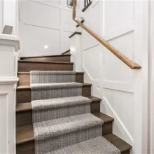 Close-up of custom staircase with wood treads, textured carpet runner, borad and batten wall pattern, and warm wood handrail.