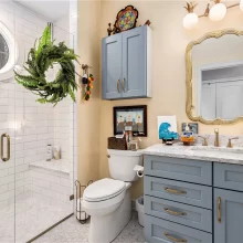 Guest bathroom with blue vanity, gold mirror, marble countertop, white subway tile walk-in shower, and glass door
