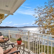Covered balcony with outdoor seating overlooking the lake, docks, and colorful autumn trees